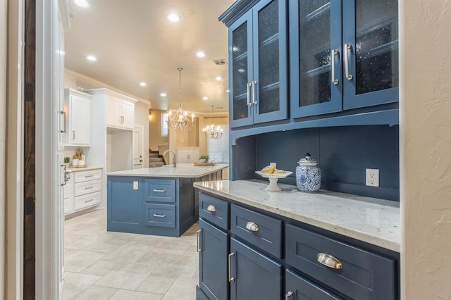 kitchen featuring blue cabinets, decorative light fixtures, a chandelier, an island with sink, and white cabinets