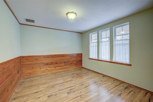 unfurnished room featuring crown molding, wooden walls, and light wood-type flooring