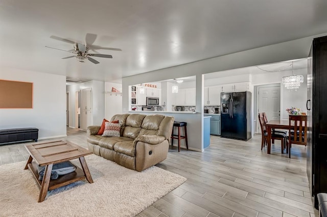 living room with ceiling fan with notable chandelier and light hardwood / wood-style flooring