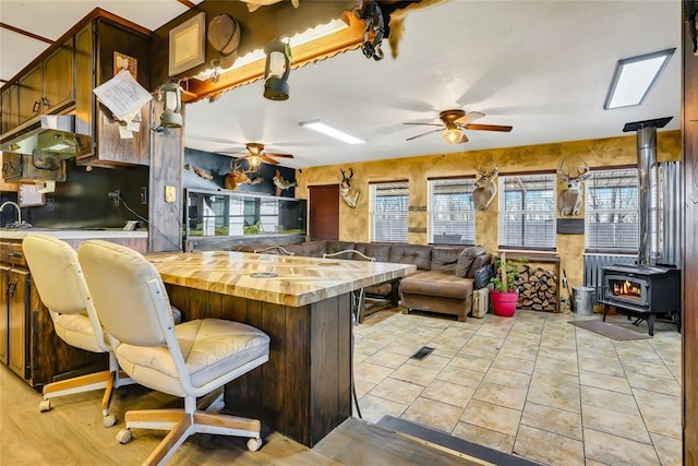 kitchen with light tile patterned flooring, a wood stove, wooden counters, a kitchen breakfast bar, and ceiling fan