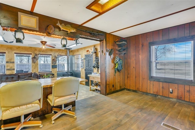 dining room featuring light hardwood / wood-style flooring, wooden walls, and ceiling fan