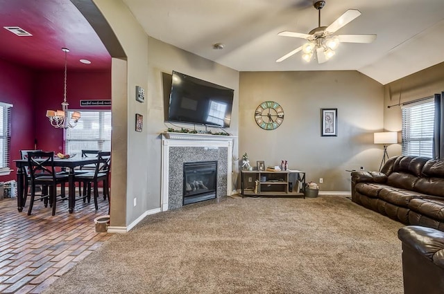 living room with a tiled fireplace, vaulted ceiling, carpet flooring, and ceiling fan with notable chandelier