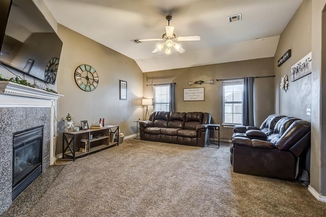 carpeted living room with a tiled fireplace, vaulted ceiling, and ceiling fan