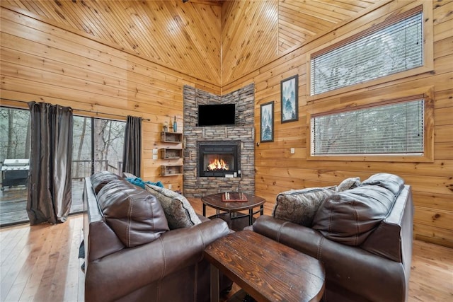 living room with light hardwood / wood-style flooring, a fireplace, wooden walls, and a high ceiling