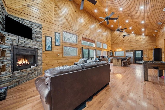 living room with a stone fireplace, high vaulted ceiling, wood walls, wood ceiling, and light hardwood / wood-style floors