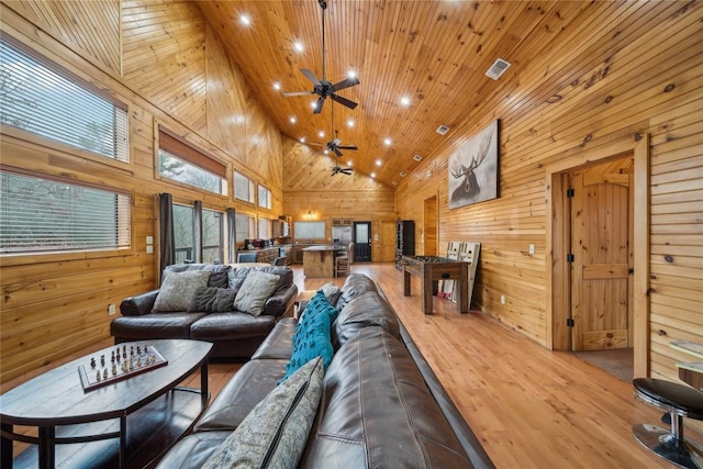 living room with high vaulted ceiling, wooden walls, wood-type flooring, ceiling fan, and wooden ceiling