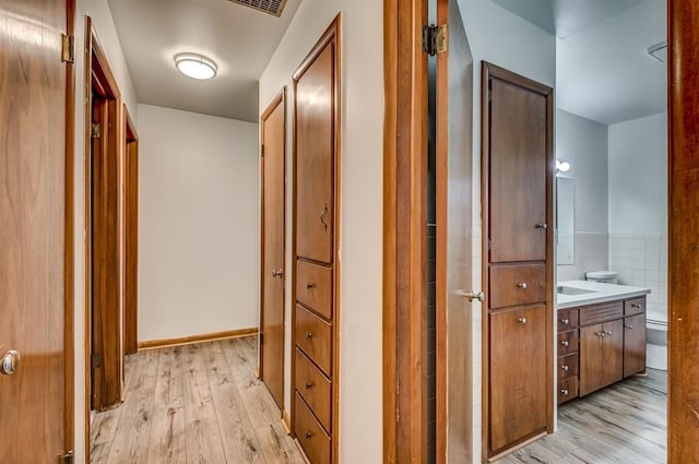 hallway featuring tile walls, sink, and light wood-type flooring