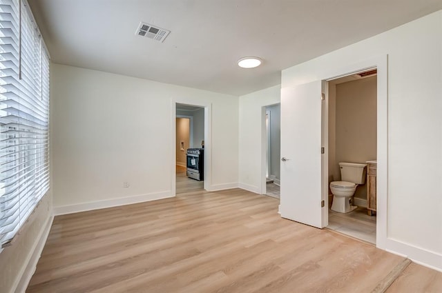 unfurnished bedroom featuring ensuite bath and light hardwood / wood-style floors