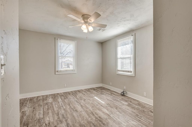 spare room featuring ceiling fan, light wood-type flooring, and a wealth of natural light