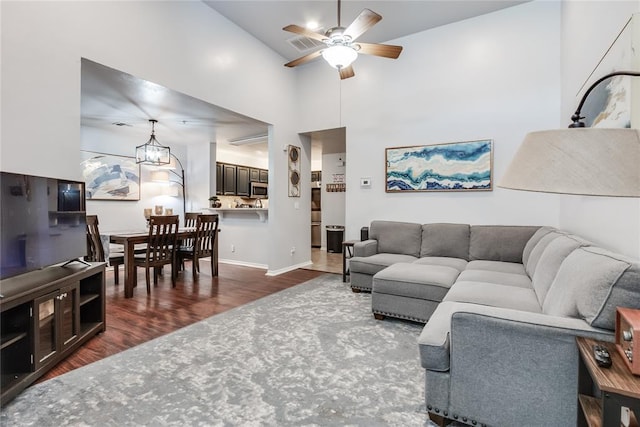 living room featuring a towering ceiling, ceiling fan with notable chandelier, and dark hardwood / wood-style flooring