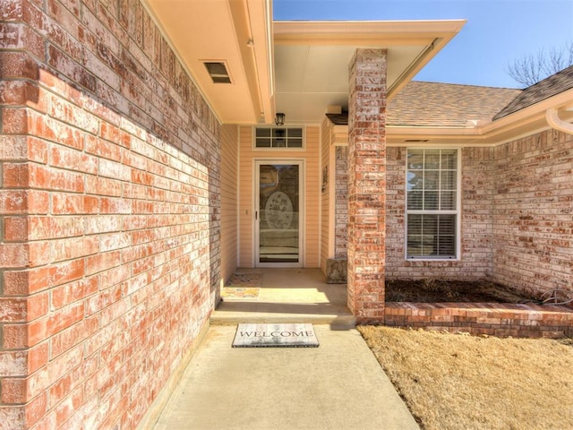 view of exterior entry with a shingled roof and brick siding