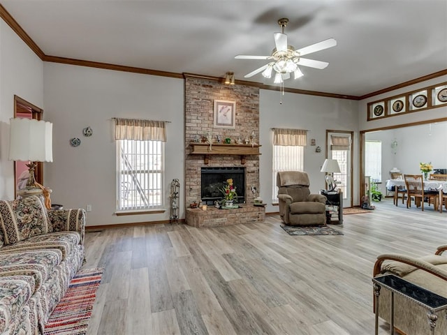 living area featuring light wood-style flooring, a fireplace, a ceiling fan, baseboards, and ornamental molding