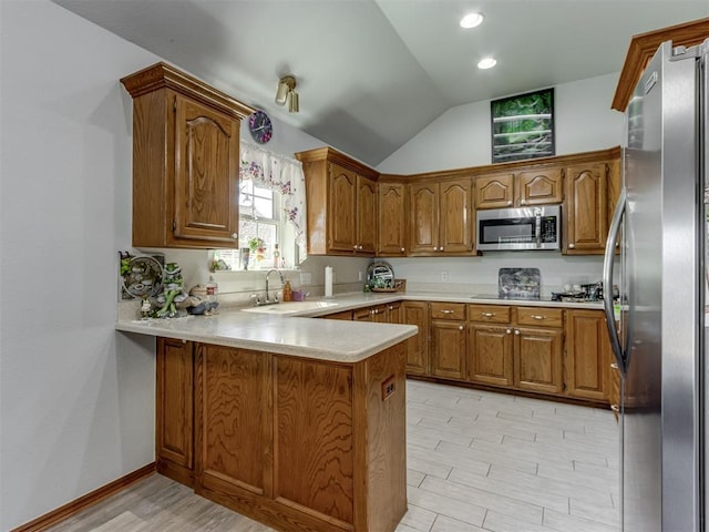 kitchen featuring a peninsula, appliances with stainless steel finishes, brown cabinetry, and a sink