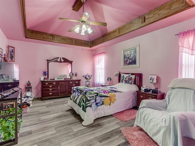 bedroom with light wood finished floors, a raised ceiling, and a ceiling fan