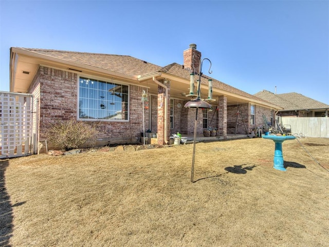 back of house with brick siding, a yard, a chimney, a shingled roof, and fence