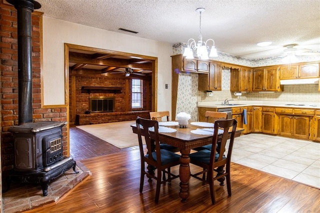 dining room featuring sink, a wood stove, a textured ceiling, ceiling fan with notable chandelier, and light wood-type flooring