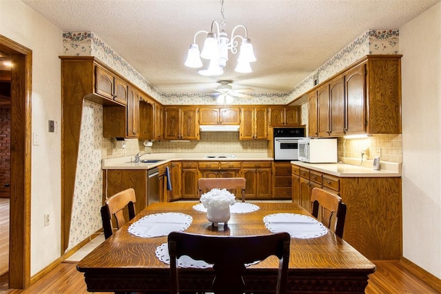 kitchen featuring sink, white appliances, hanging light fixtures, light hardwood / wood-style floors, and decorative backsplash