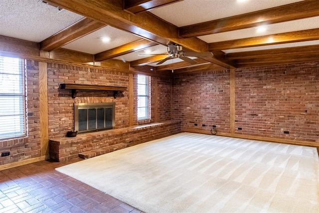 unfurnished living room with ceiling fan, a textured ceiling, brick wall, a brick fireplace, and beamed ceiling