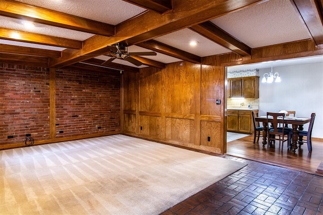 living room with brick wall, ceiling fan with notable chandelier, wooden walls, beamed ceiling, and a textured ceiling