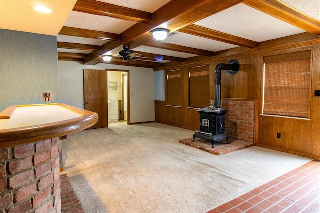 living room with carpet flooring, beam ceiling, a wood stove, and wood walls