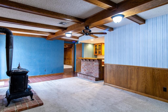 unfurnished living room featuring wooden walls, a wood stove, carpet, ceiling fan, and a textured ceiling