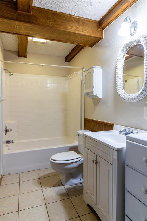 full bathroom with toilet, a textured ceiling, vanity, tiled shower / bath combo, and tile patterned flooring