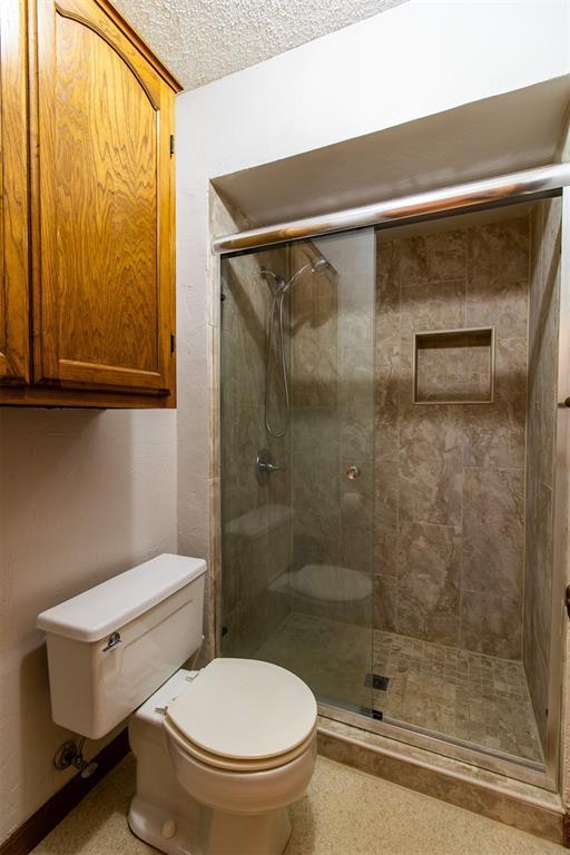 bathroom featuring an enclosed shower, a textured ceiling, and toilet