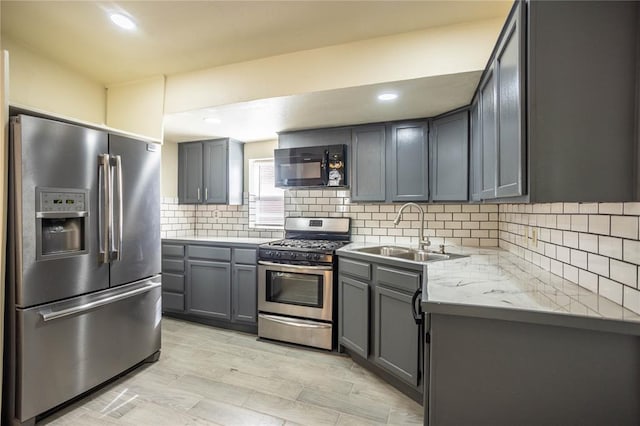 kitchen with sink, appliances with stainless steel finishes, gray cabinetry, tasteful backsplash, and light stone countertops