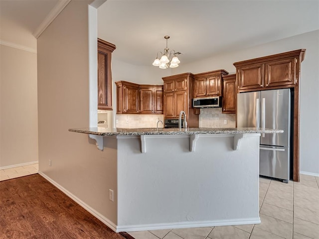 kitchen featuring a breakfast bar area, decorative backsplash, kitchen peninsula, stainless steel appliances, and an inviting chandelier