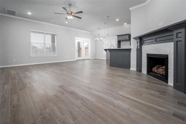 unfurnished living room featuring dark wood-type flooring, ornamental molding, a fireplace, and ceiling fan with notable chandelier