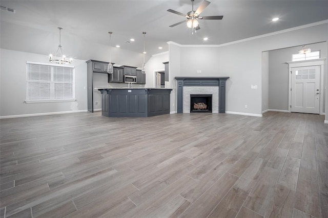 unfurnished living room featuring hardwood / wood-style floors, crown molding, ceiling fan with notable chandelier, and a fireplace