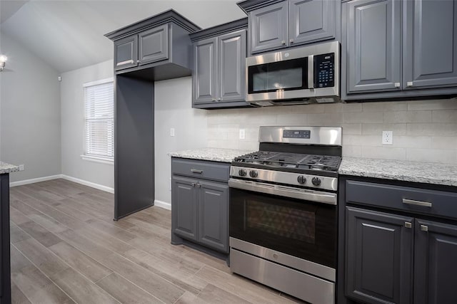 kitchen with stainless steel appliances, tasteful backsplash, light stone countertops, and light wood-type flooring