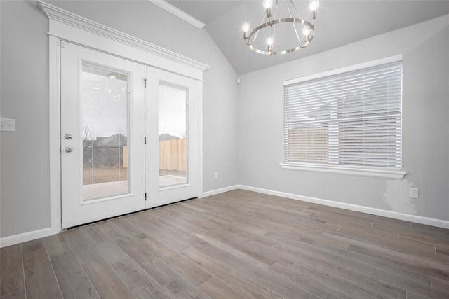 empty room featuring vaulted ceiling, plenty of natural light, a chandelier, and light hardwood / wood-style flooring