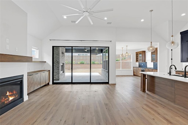 unfurnished living room with sink, a notable chandelier, high vaulted ceiling, and light hardwood / wood-style flooring