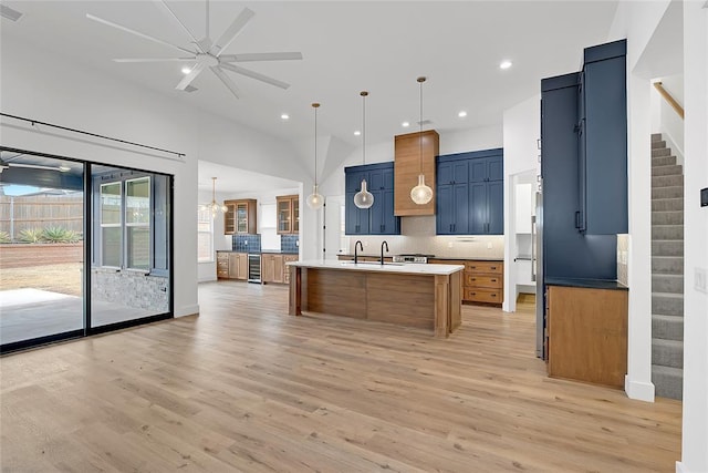 kitchen with a kitchen island with sink, pendant lighting, backsplash, and light wood-type flooring