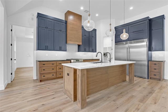 kitchen with decorative light fixtures, a center island with sink, stainless steel appliances, light stone countertops, and light hardwood / wood-style floors