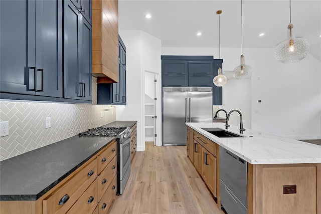 kitchen featuring sink, appliances with stainless steel finishes, decorative light fixtures, dark stone counters, and a large island with sink