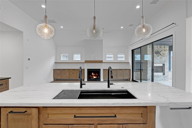 kitchen with vaulted ceiling, light stone countertops, sink, and decorative light fixtures