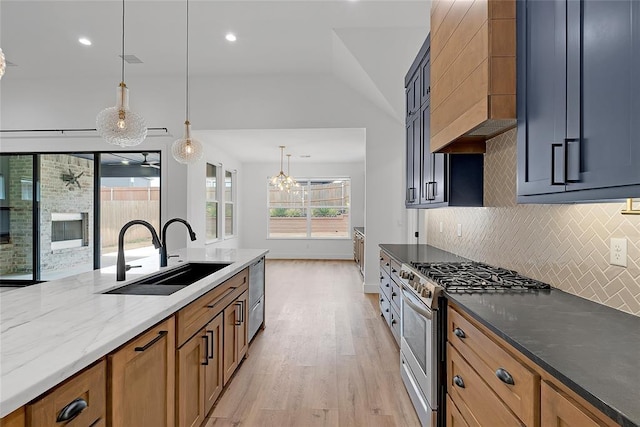 kitchen featuring pendant lighting, sink, wall chimney range hood, stainless steel appliances, and light stone counters