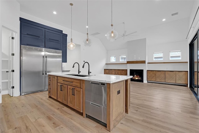 kitchen featuring sink, light stone counters, a center island with sink, appliances with stainless steel finishes, and pendant lighting