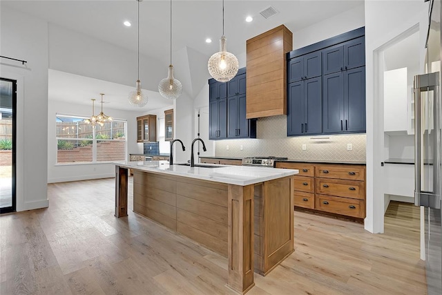 kitchen featuring blue cabinetry, sink, a center island with sink, pendant lighting, and light stone countertops