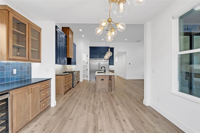 kitchen featuring stainless steel range with gas cooktop, decorative light fixtures, a kitchen bar, a kitchen island with sink, and light wood-type flooring