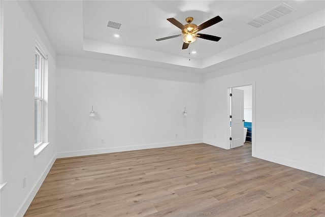 spare room with a tray ceiling, light hardwood / wood-style flooring, and ceiling fan