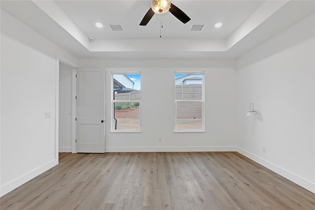 spare room with ceiling fan, a tray ceiling, and light hardwood / wood-style floors