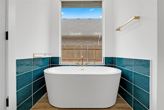 bathroom with a washtub, hardwood / wood-style floors, and tile walls