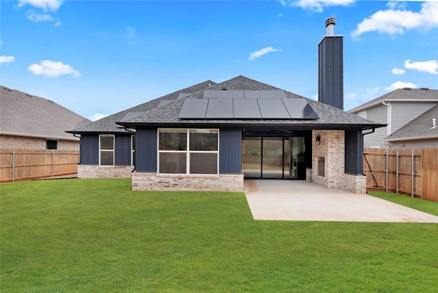 rear view of house featuring a patio, a yard, and solar panels