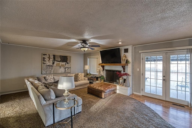 living room featuring french doors, ornamental molding, hardwood / wood-style flooring, ceiling fan, and a fireplace