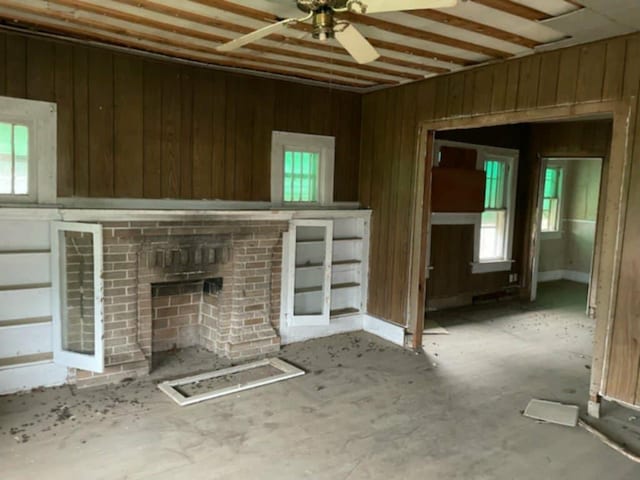 unfurnished living room featuring ceiling fan, a brick fireplace, and wooden walls