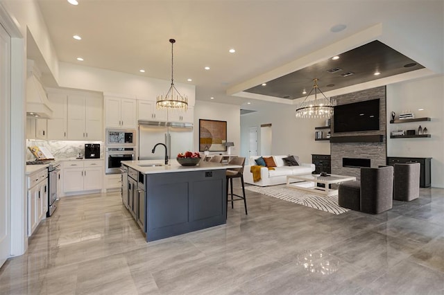 kitchen featuring built in appliances, white cabinets, a notable chandelier, and a fireplace