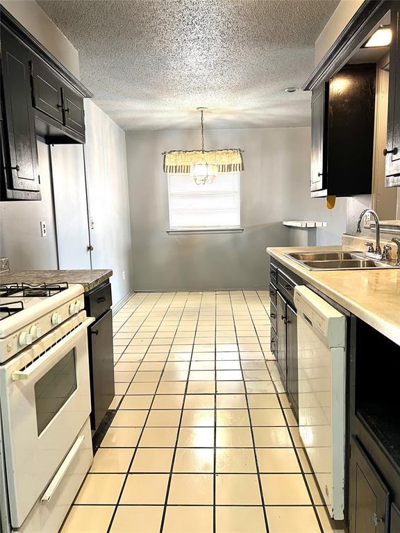 kitchen with pendant lighting, sink, white appliances, light tile patterned floors, and a textured ceiling